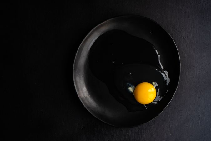 Cracked raw egg on dark plate
