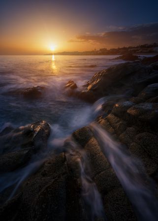 Sea waving near rough rocks during sunset