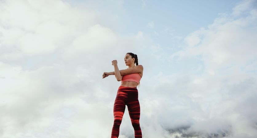 Muscular female stretching arms against sky