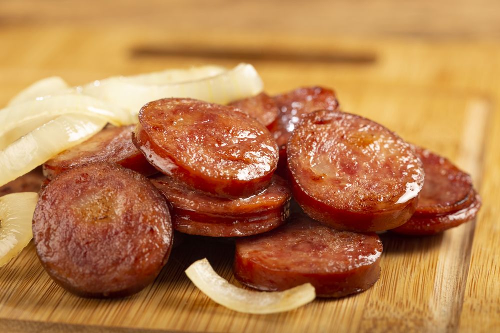 Sliced calabrese sausage with onion on wooden background.