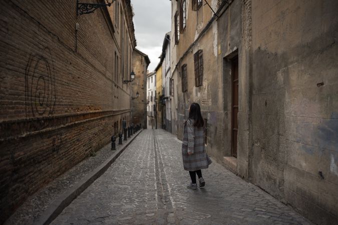 Woman walking on aged empty alleyway with old buildings