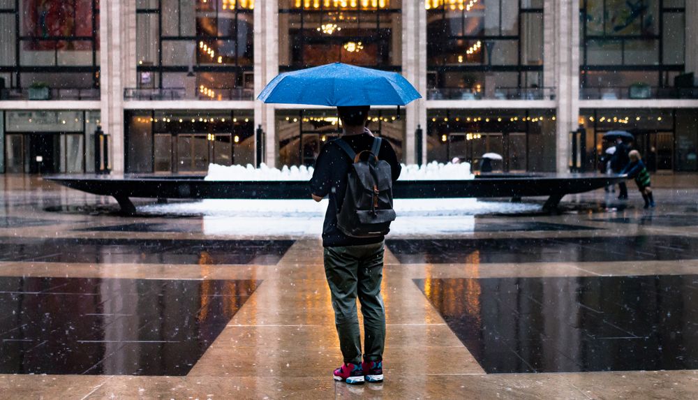 Back view of man holding a blue umbrella standing near fountain