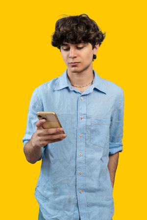 Young man using a smartphone on a vibrant yellow background.