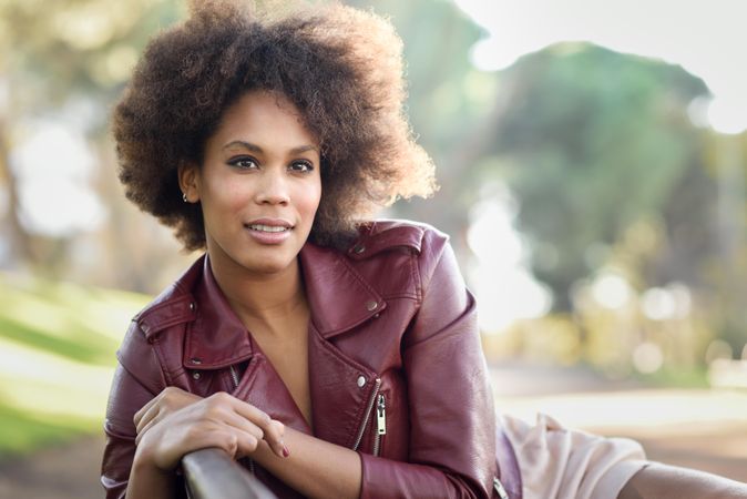 Calm woman sitting outside in red leather jacket looking at camera