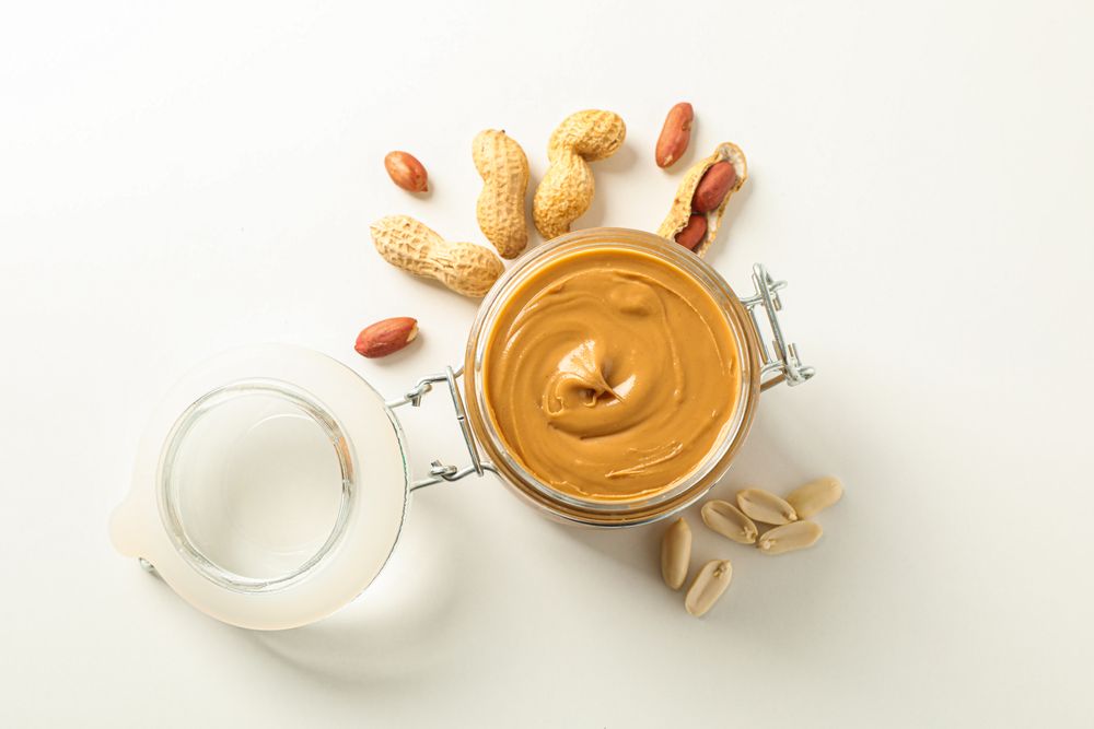 Flat lay composition with glass jar with peanut butter and peanut on light background, space for text and top view