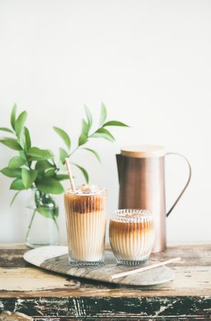 Two glasses of iced coffee and a pitcher, with light background with leaves