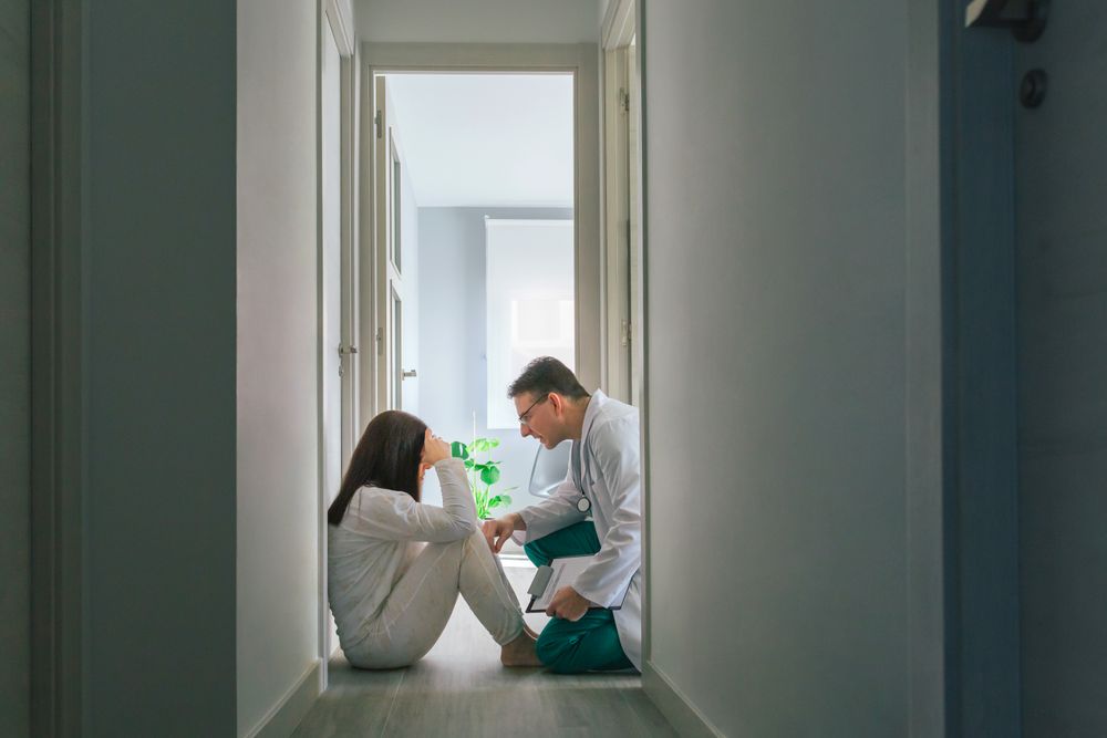 Doctor reassuring with empathy a patient sitting on the floor of a mental health center