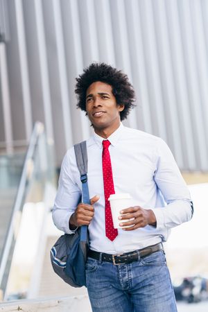 Man wearing tie holding a cup of coffee walking to work