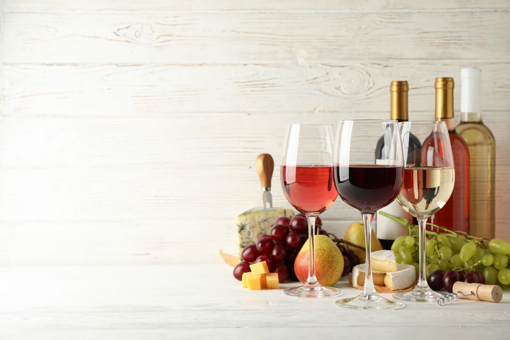 Fruits, cheese, bottles and glasses with different wine on light background, space for text