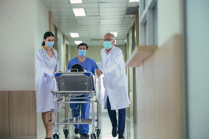 Group of medical staff wheeling patient in bed through hospital hallway
