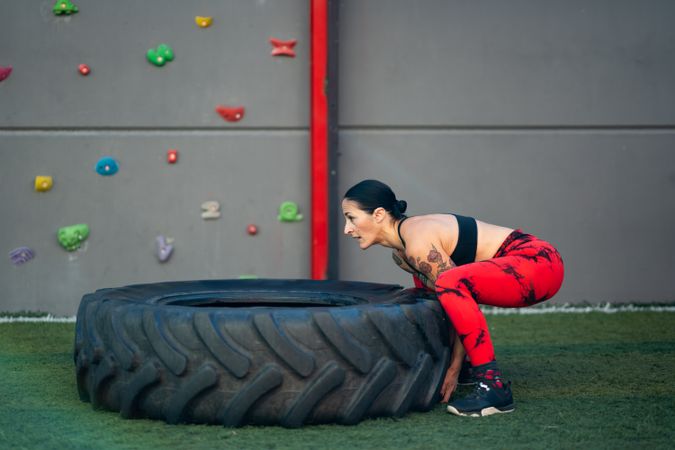 Side view of fit woman lifting a truck wheel in a gym