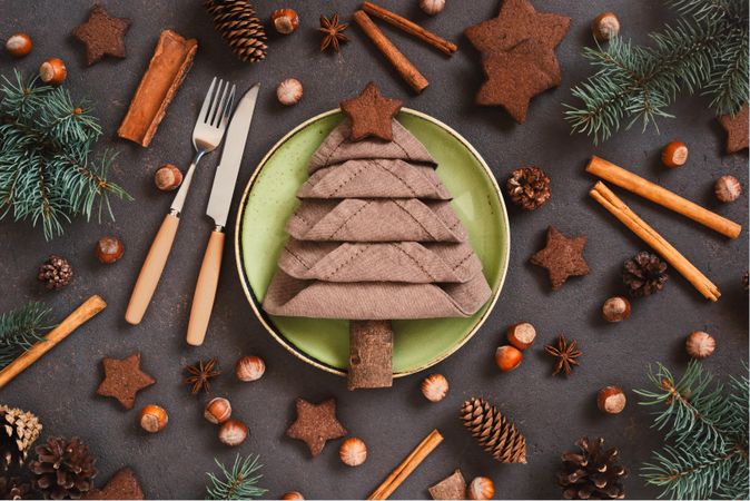 Holiday table setting with napkin in the shape of a tree, surrounded by cookies and holiday spices