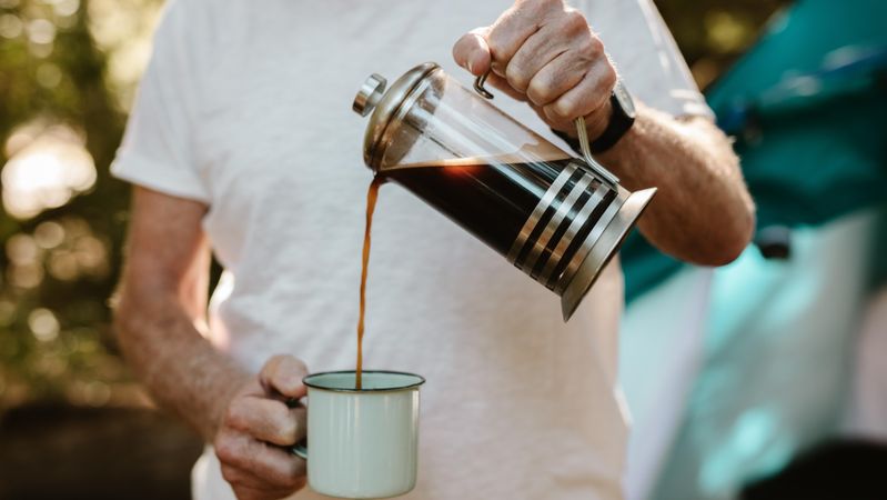 Close-up of a mature man pouring coffee in a mug at campsite