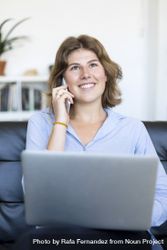 Businesswoman sitting on sofa at home using a laptop and speaking on phone 48BJej