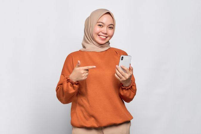 Cheerful Muslim woman pointing at her smartphone