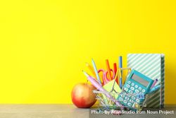 Basket of back to school supplies on desk with yellow wall 5zMdg0