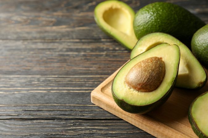 Board with avocado on wooden background, close up