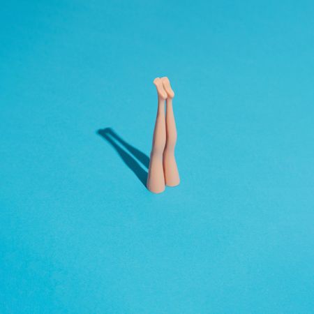 Doll legs sticking upright from blue background with shadow