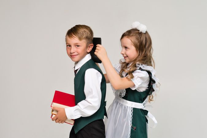 Two elementary school students in uniform with books and tablet