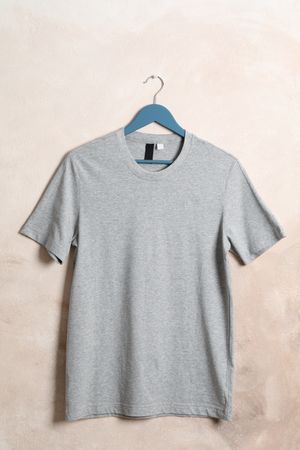 Hanger with blank gray t-shirt on light brown background, space for text
