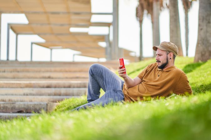 Relaxed man lying on the grass using the phone