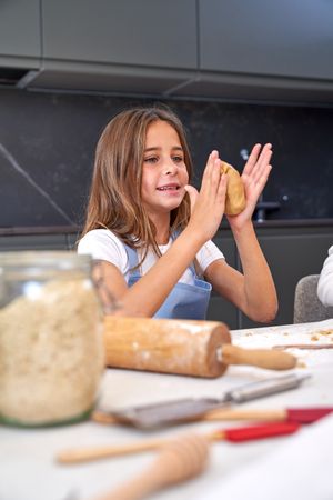 Smiling little girl kneading dough with hands in kitchen