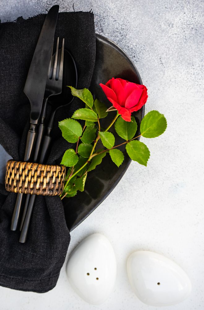 Table setting with red rose with dark plate and cutlery