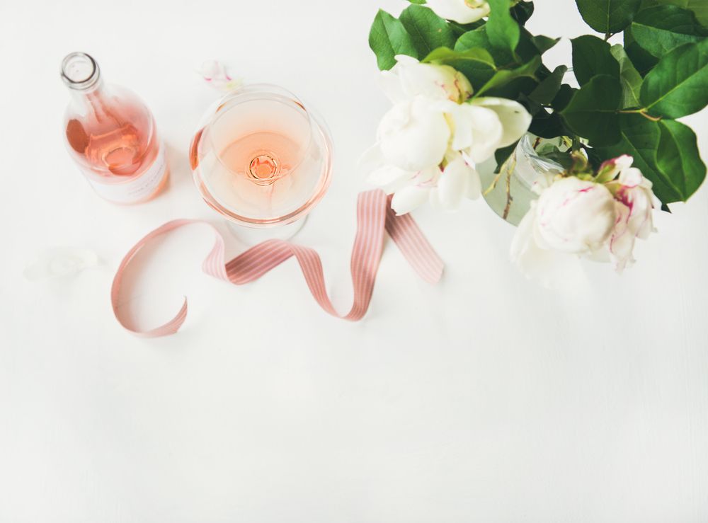 Glass of pink rose wine, and bottle with flowers and ribbon, horizontal composition with copy space