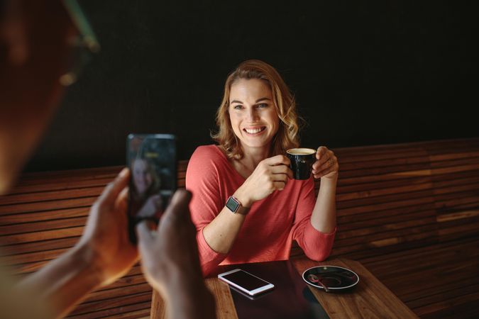 Woman sitting at a coffee table smiling for a photograph holding a coffee cup