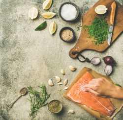 Salmon fillet being salted, fresh herbs, limes, onions, bread board, square crop, copy space