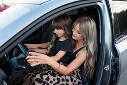 Mother teaching little daughter to drive driving car together
