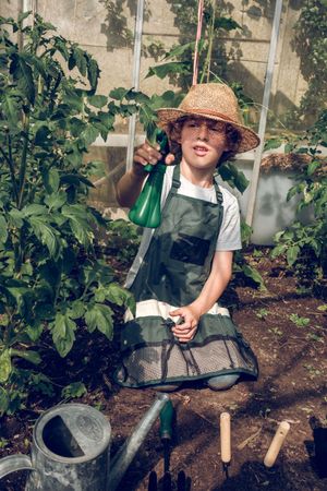 Boy irrigating plants with spray bottle in greenhouse