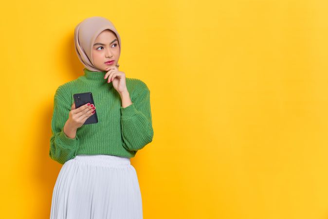 Woman in headscarf looking aside and holding smart phone