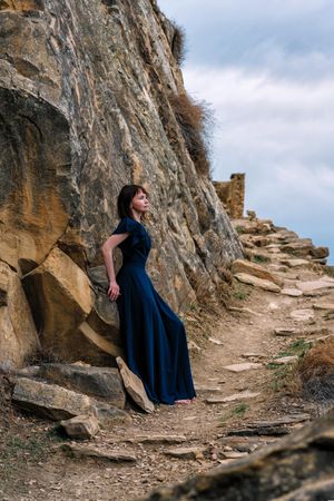 Woman in long blue dress posing on mountainous pathway
