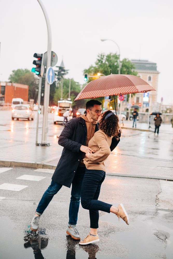 Happy couple with umbrella hugging on wet street