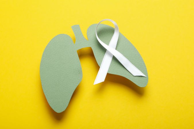 Green lungs cut out of paper with ribbon on yellow background
