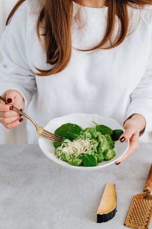 Cropped image of woman in light sweater holding a bowl of green salad