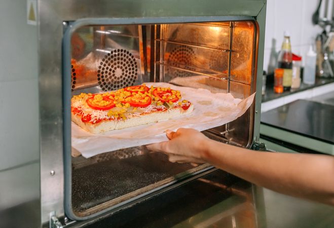 Unrecognizable professional cook putting pizza into oven in restaurant kitchen
