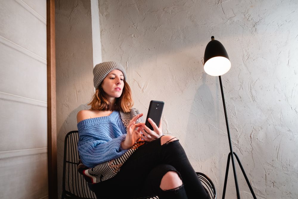 Woman in sweater and hat on the mobile phone and sitting near wall