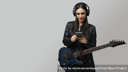 A female guitarist, enjoys listening to music with headphones from the mobile phone she holds in her hands 47mmYg