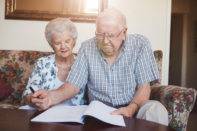 Mature man and woman sitting on sofa and signing some paperwork
