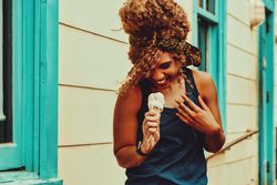 Joyous Black female snacking on an ice cream cone in the sun