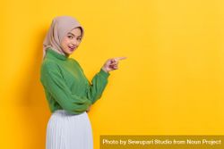 Woman in headscarf facing to the side and pointing at yellow copy space 4OAmE0