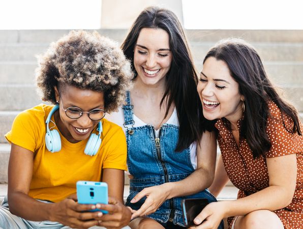 Group of female friends laughing outside looking at phone