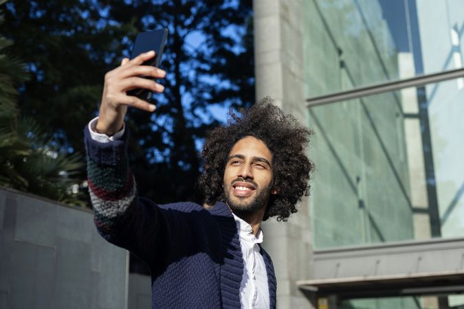 Happy Black man taking selfie with smartphone while outside in the sun