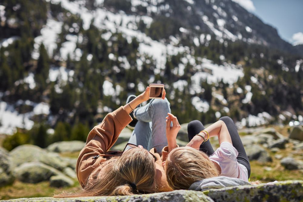 Two young women lay on a flat rock in a mountain scenery