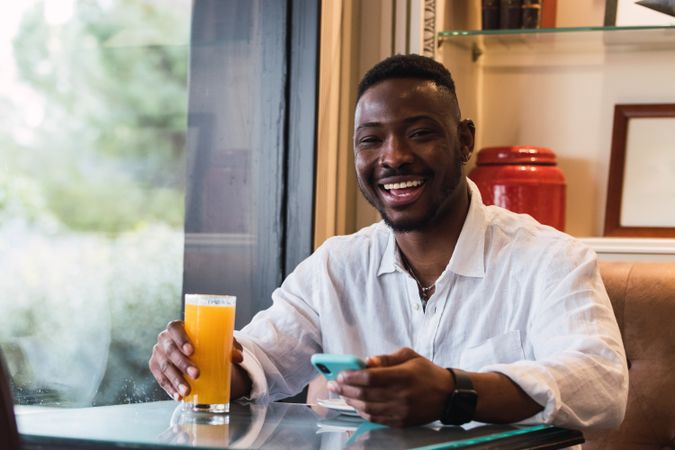 Happy Black man using smartphone in cafe while sipping an orange juice