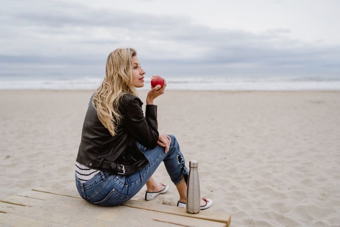 Woman eating an apple sitting on beach
