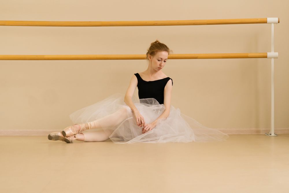 Ballet dancer adjusts her tutu while seated