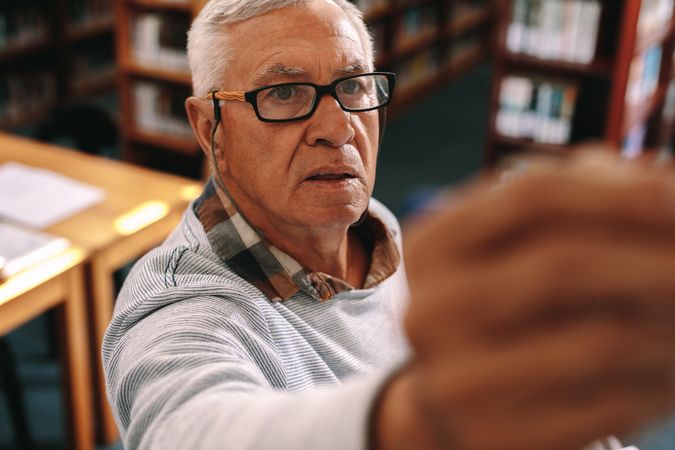 Older male reaching for book in library